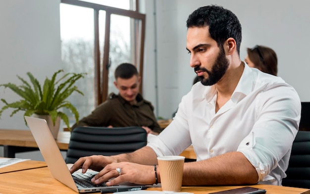 Attractive bearded man in pristine white shirt working on silver laptop in modern office