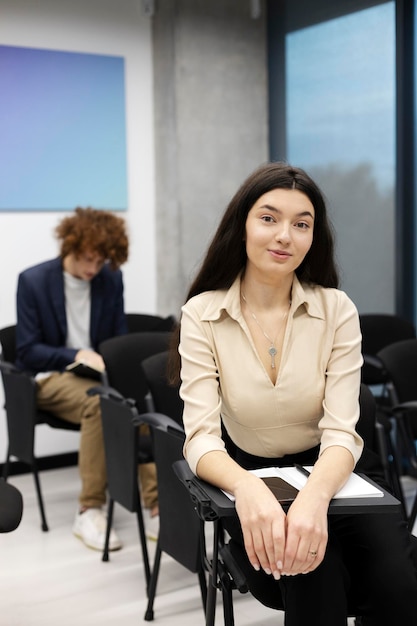 Attractive beautiful female student sitting in room for meeting studying looking at camera Smiling businesswoman writing down important things at meeting