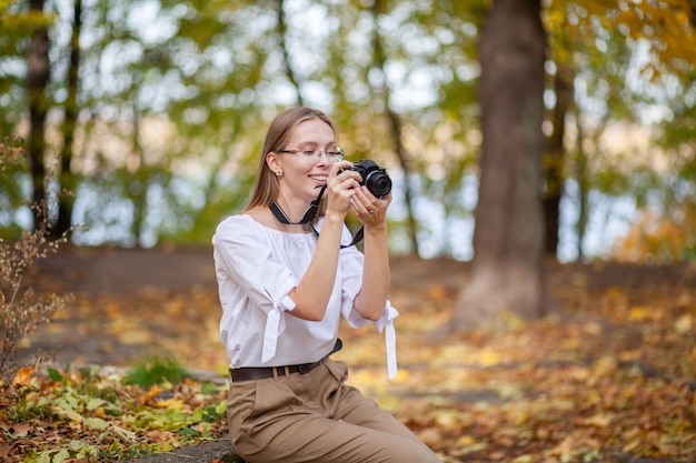 Attractive beautiful young girl holding modern mirror-less camera in autumn park