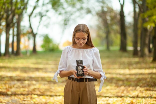 Attractive beautiful young girl holding retro vintage twin lens reflection camera in autumn park