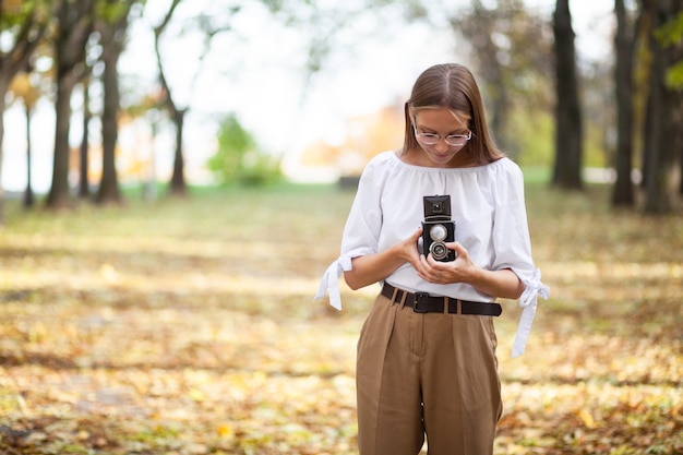 Attractive beautiful young girl holding retro vintage twin lens reflection camera in autumn park