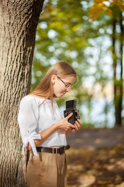 Photo attractive beautiful young girl holding retro vintage twin lens reflection camera in autumn park