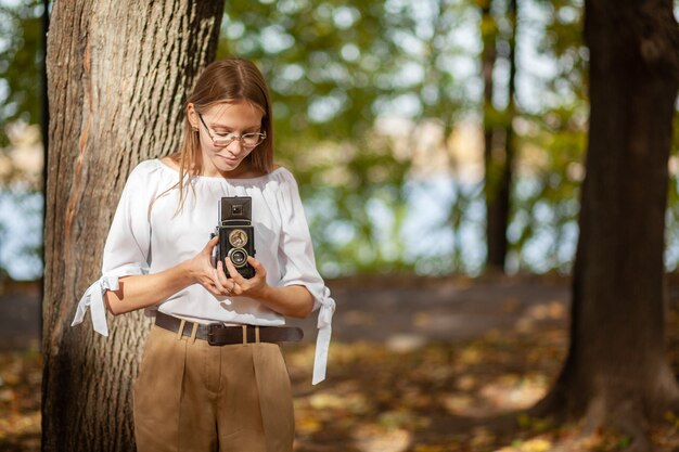 Attractive beautiful young girl holding retro vintage twin lens reflection camera in autumn park