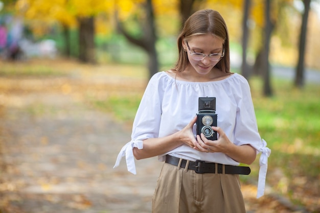 Attractive beautiful young girl holding retro vintage twin lens reflection camera in autumn park