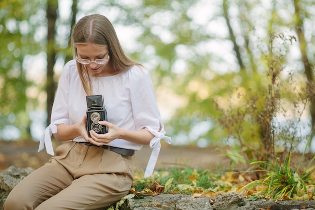 Attractive beautiful young girl holding retro vintage twin lens reflection camera in autumn park