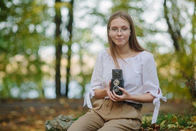 Attractive beautiful young girl holding retro vintage twin lens reflection camera in autumn park