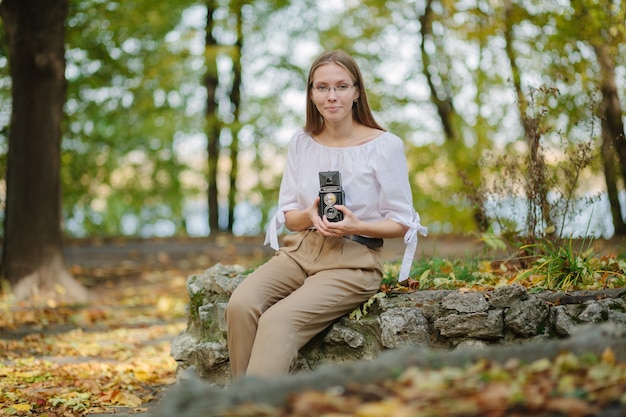 Attractive beautiful young girl holding retro vintage twin lens reflection camera in autumn park