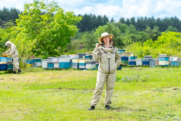 Attractive beekeeper working in apiary Attractive woman in beekeeper hat staying near hive and smiling to the camera Occupation concept