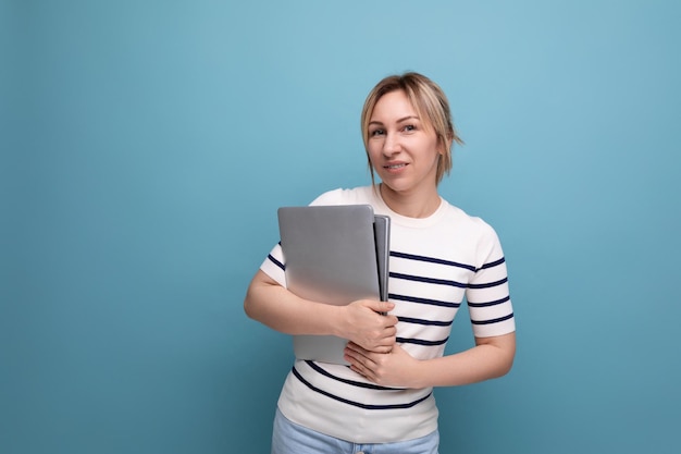 Attractive blond girl student in a casual outfit with a laptop in her hands on a blue background