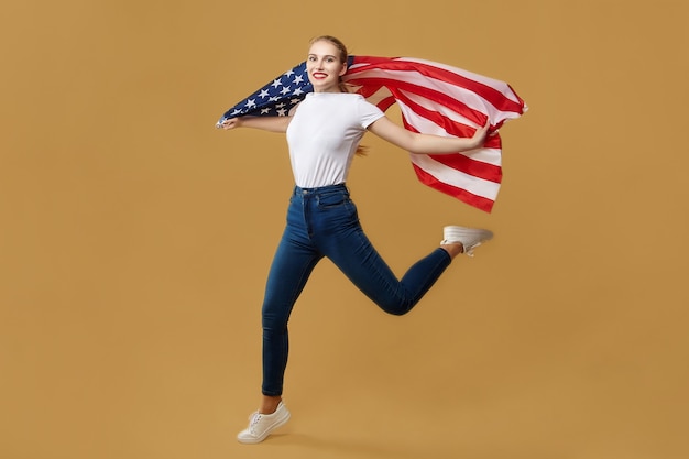 Attractive blonde made a jump with an American flag. photo shoot in the studio on a yellow background.