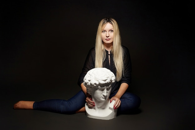 Attractive blonde posing with a bust of David. photo shoot in the studio on a black background