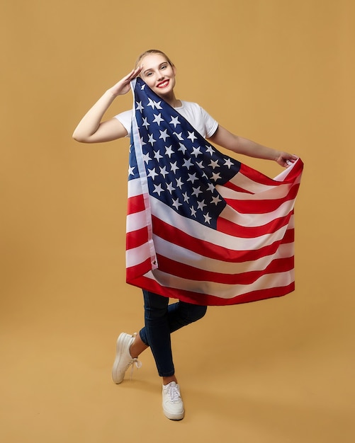 Attractive blonde proudly poses with an American flag. photo shoot in the studio on a yellow background.