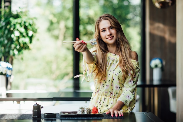 Attractive, blonde woman in chinese restaurant with sushi rolls posing and smiling