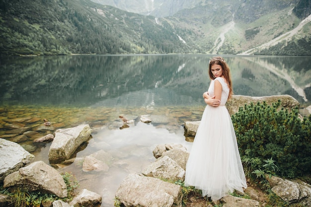 Attractive brunette bride in gorgeous white wedding dress standing near the lake Morskie Oko