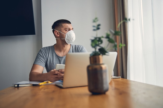 Attractive brunette male sitting in front of computer in living room while looking in window