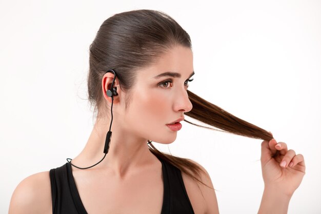 Attractive brunette woman in jogging black top listening to music on earphones posing 