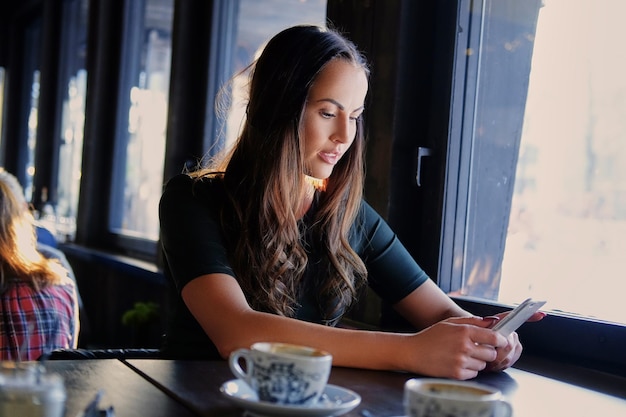 Attractive brunette woman texting an SMS in a cafe.