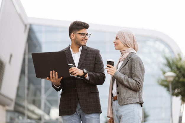 Attractive business couple of arab man and Muslim woman in smart casual style standing outside office