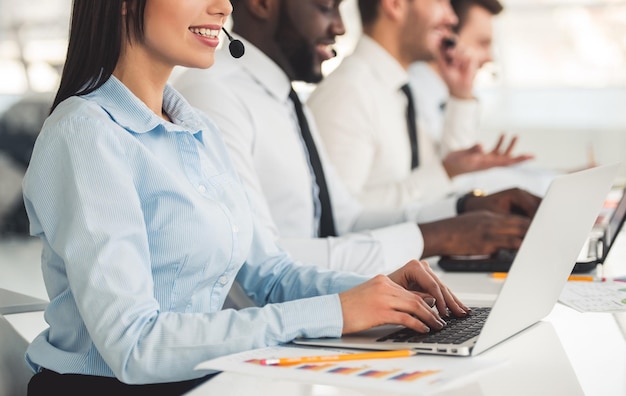 Attractive business people in suits and headsets are smiling while working with laptops in office