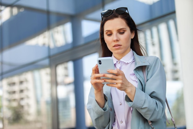 Attractive business woman carefully looks into the smartphone screen on the background of the business center