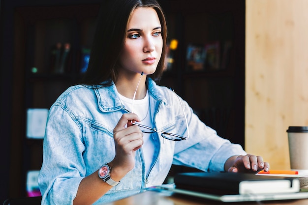 Attractive business woman is sitting at table in front of laptop. Beautiful brunette woman, holds glasses