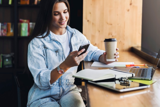 Attractive business woman sits at table in front of laptop and talks on mobile phone, negotiates on the phone.