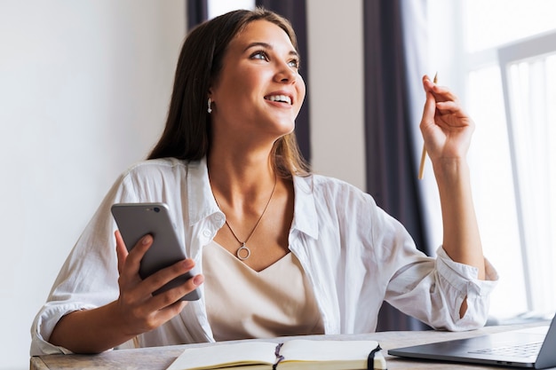 Attractive business woman sits at table in front of laptop and talks on mobile phone, negotiates on the phone.