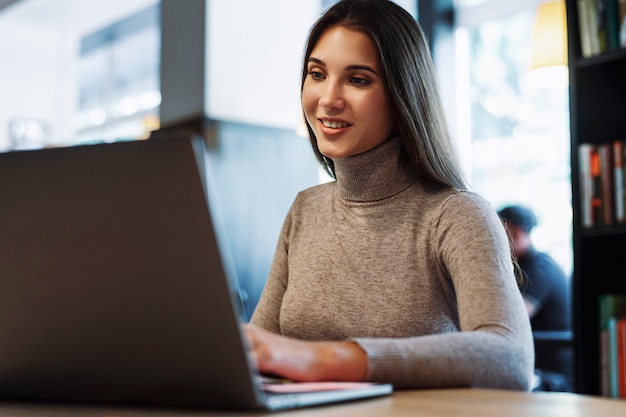 Attractive business woman sits at table in front of laptop, works remotely while in cafe.