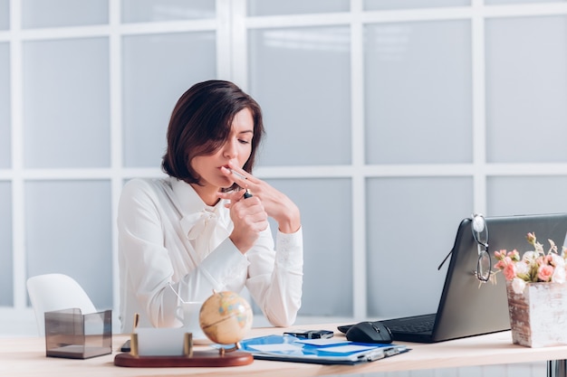 Attractive business woman  smokes and works at the desk in the office