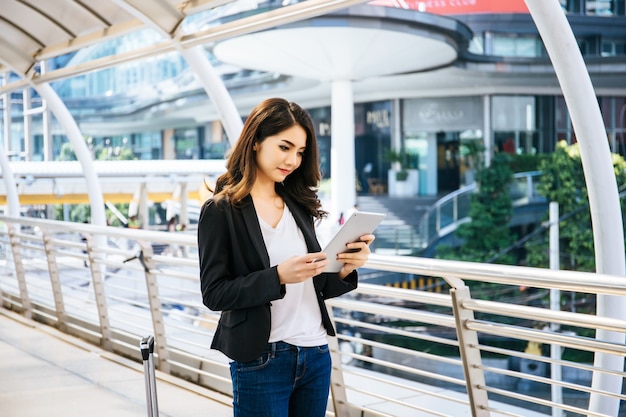 Attractive business woman using a digital tablet while standing in front of office building.