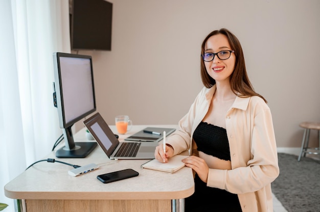 Attractive business woman wearing casual clothes working at home office on laptop and making notes Young happy female student studying in online university