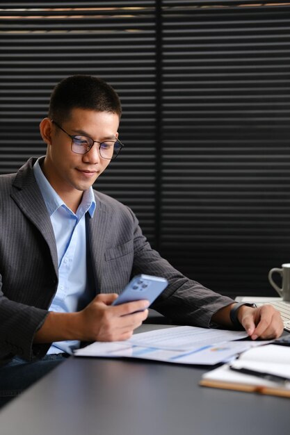 Attractive businessman checking social media on smartphone at office desk People technology and lifestyle