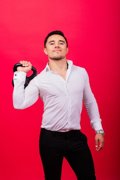 Attractive businessman exercising with kettlebell in studio red background