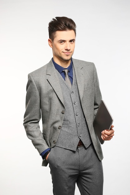 Attractive businessman smiling and holding his tablet while wearing a red tie and blue suit standing on white studio background