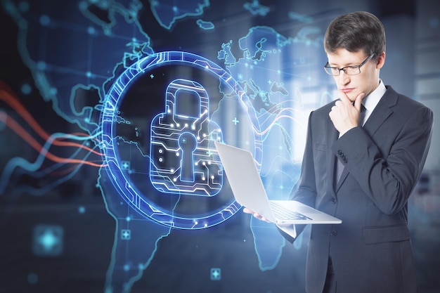 Attractive businessman using laptop with abstract digital padlock and map hologram on blurry office interior background Security and global protection concept Double exposure