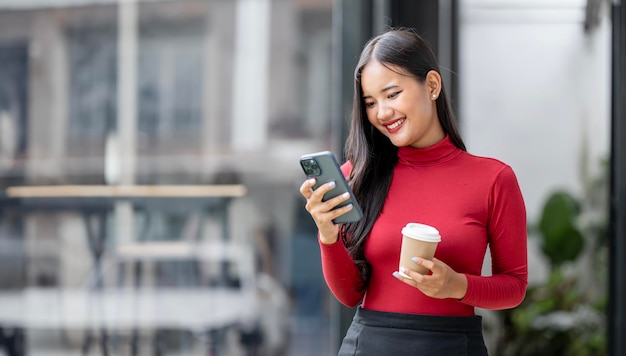 Attractive businesswoman drinking a coffee and using mobile phone while standing outdoors