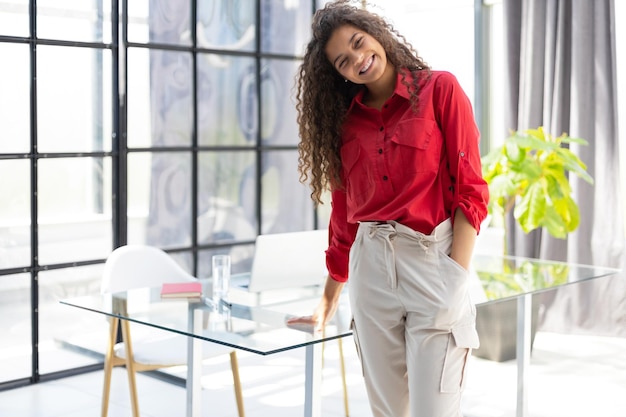 Attractive businesswoman in red shirt looking at camera while standing in the office