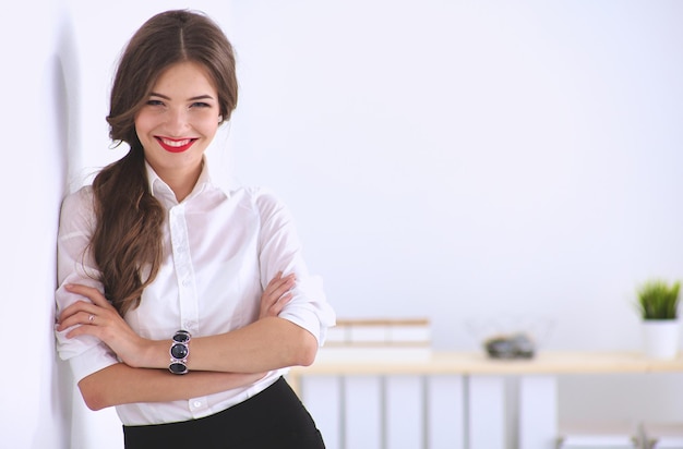 Attractive businesswoman standing near wall in office