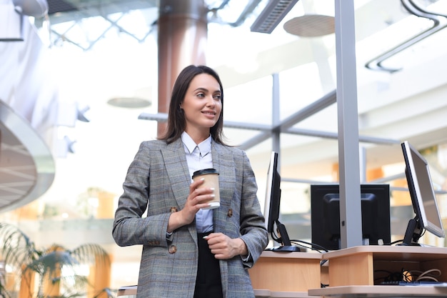 Attractive businesswoman standing with coffee near desk in the office.