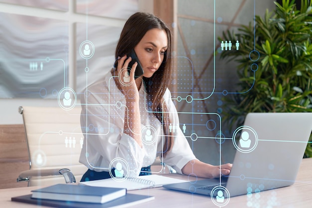 Attractive businesswoman in white shirt has conference call to hire new employees for international business consulting HR social media hologram icons over office background