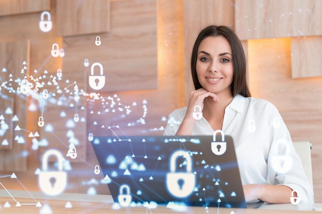 Attractive businesswoman in white shirt at workplace working with laptop to defend customer cyber security Concept of clients information protection Padlock hologram over office background