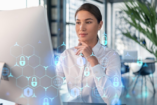 Attractive businesswoman in white shirt at workplace working with laptop to defend customer cyber security Concept of clients information protection Padlock hologram over office background