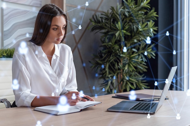 Attractive businesswoman in white shirt at workplace working with laptop to hire new employees for international business consulting HR social media hologram icons over office background