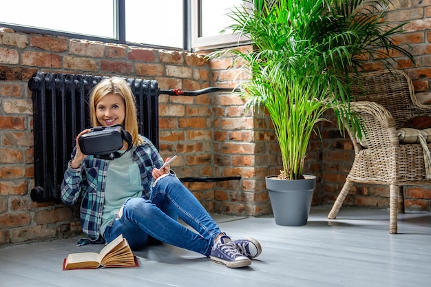 Attractive casual blond female sitting on the floor and reading a book in living room.