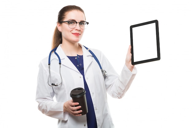 Attractive caucasian brunette confident female doctor standing in office with cup of coffee showing tablet in her hands