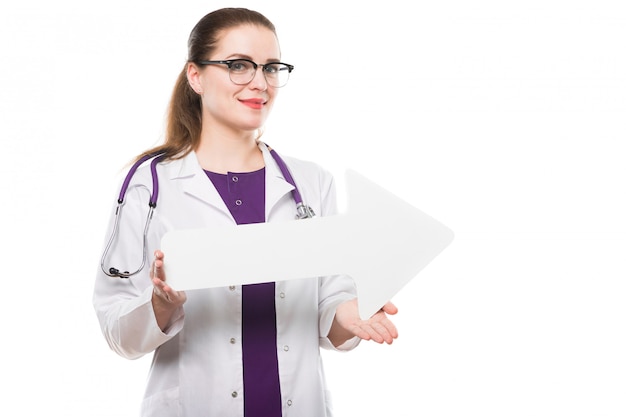 Attractive caucasian brunette female doctor standing in office smiling with paper arrow in her hands