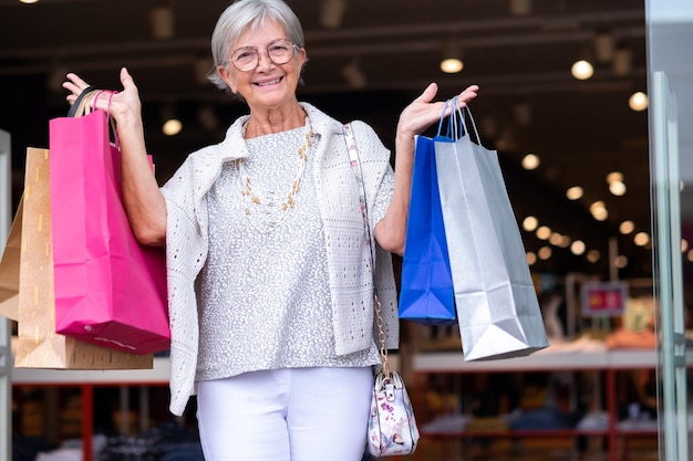 Attractive caucasian elderly woman holding shopping bags as she walks out of a store enjoying shopping consumerism concept