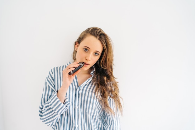 attractive caucasian female against white wall She is using a electronic cigar