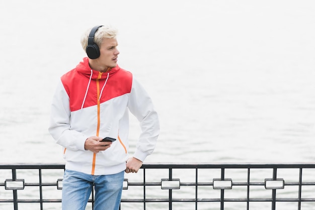 Attractive Caucasian man athlete relax after workout outdoor messaging via social networks at smart phone and using headphones for listening to music Healthy lifestyle and people concept