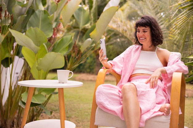 Attractive caucasian young brunette girl communicates by video communication through phone sitting in backyard of house Concept of positive emotions technology